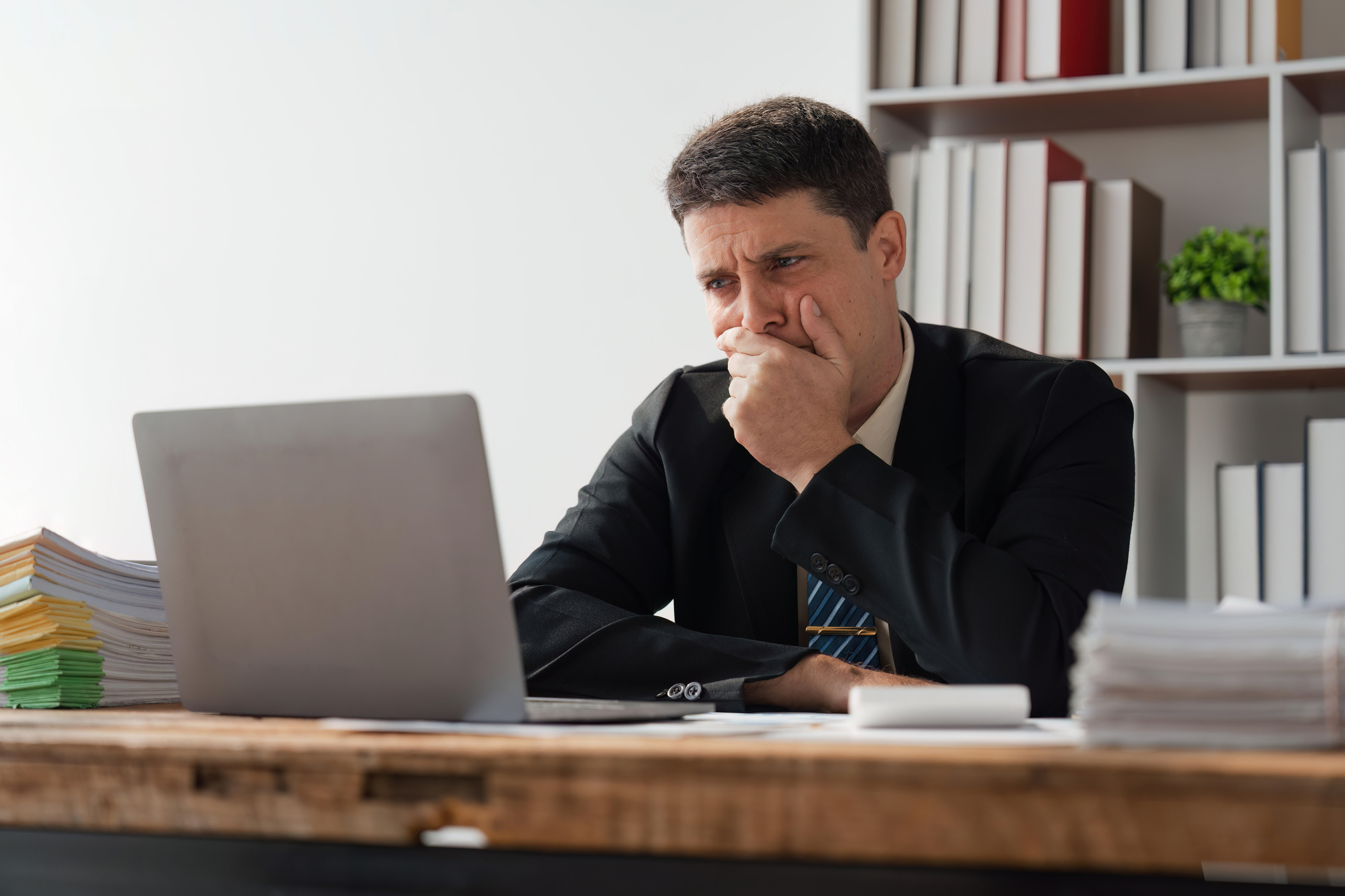 Thoughtful young businessman staring at laptop, puzzled, unsure look, distracted from analyzing tasks Have a question or challenge feel uncertain